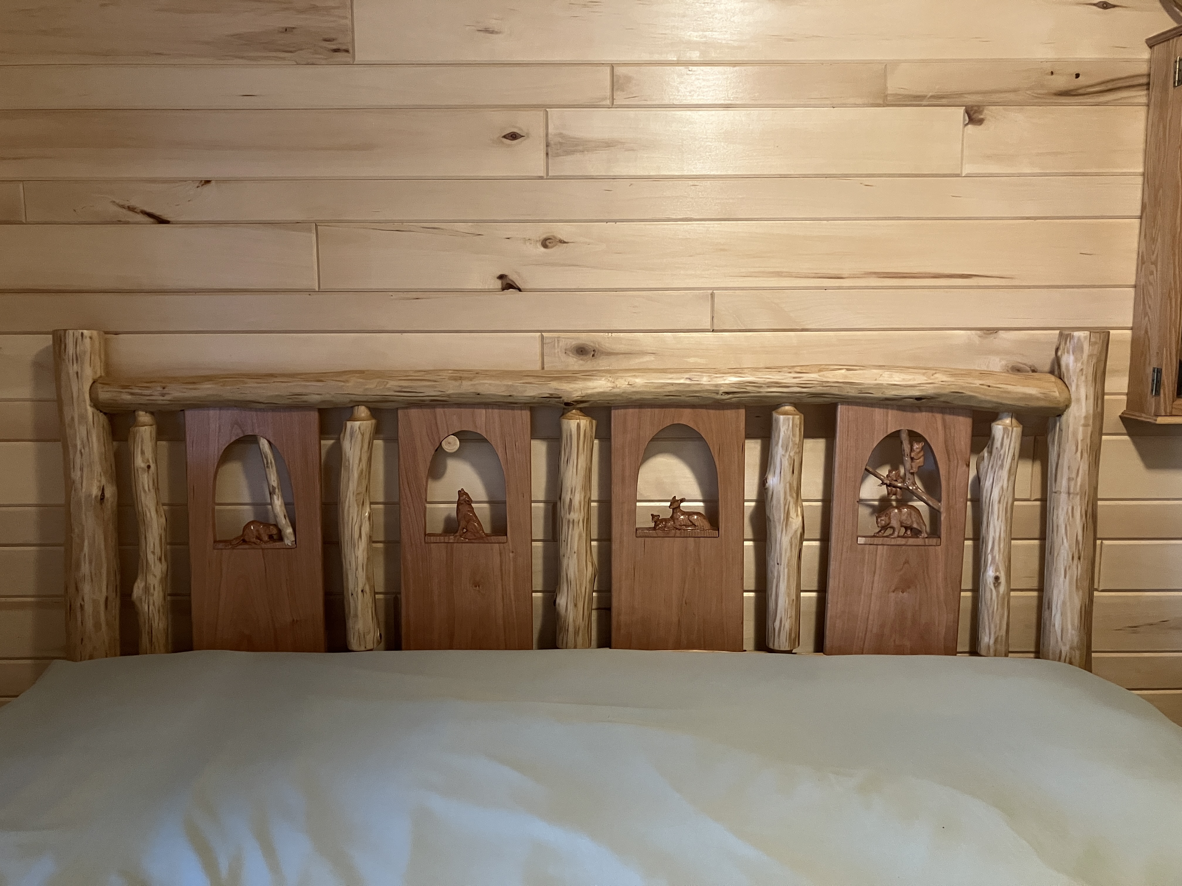 Front view of log headboard with wildlife carving panel on sage green bedding