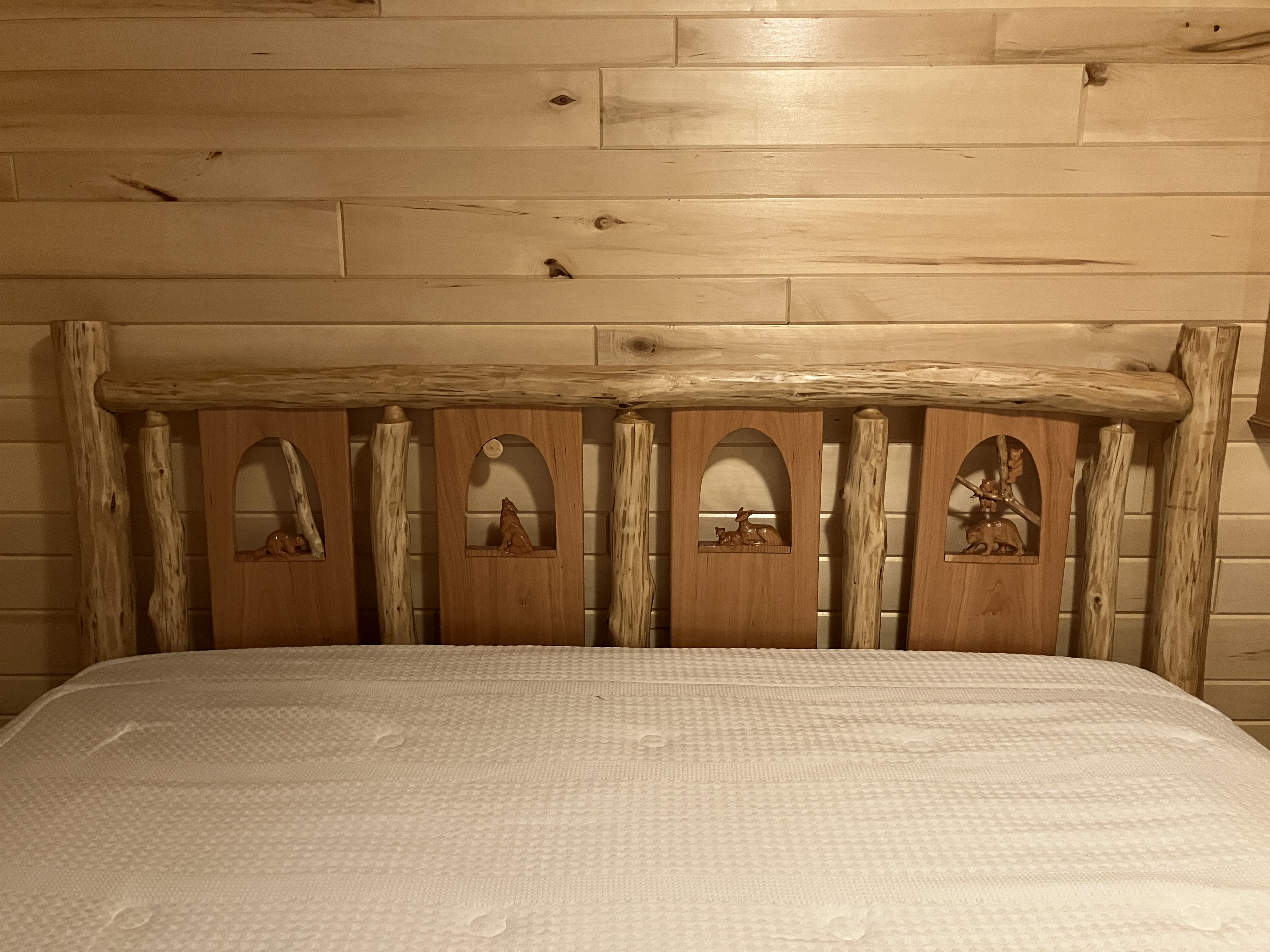 Front view of log headboard with wildlife carving panel on white bedding