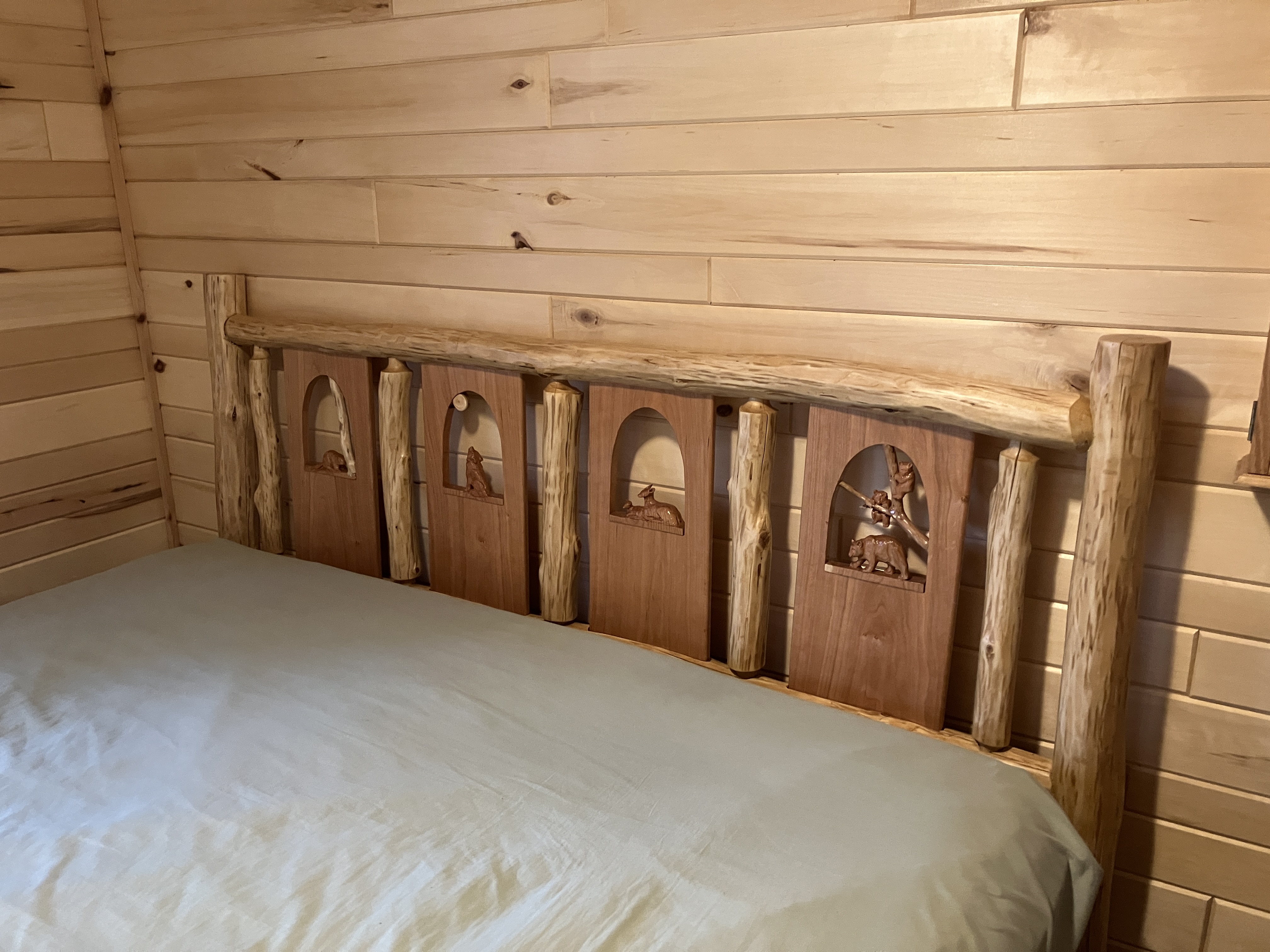 Right-side angle of log headboard with sage bedding showing contrast between logs and carving